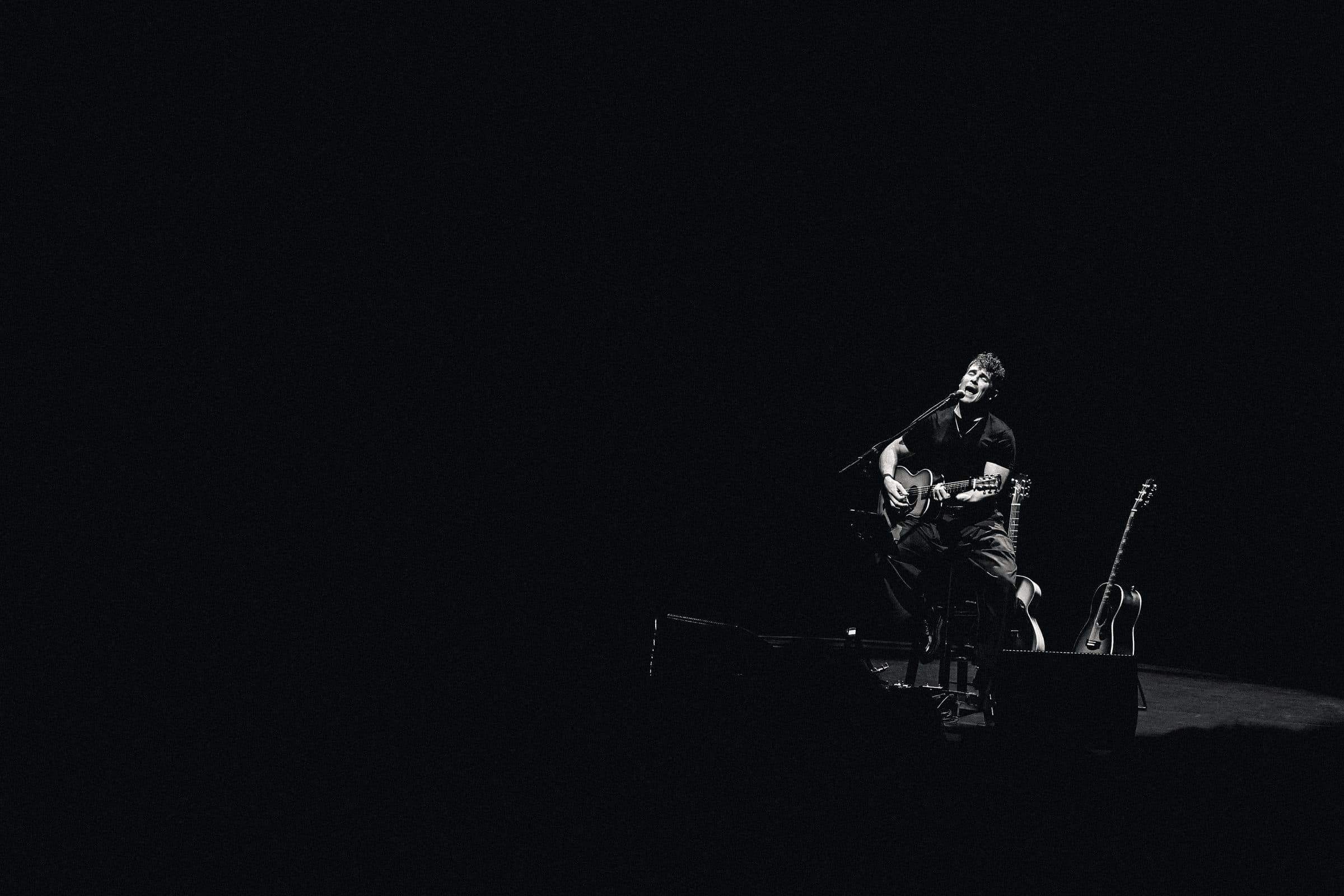 Wide stage frame of a musician under theatre lights.