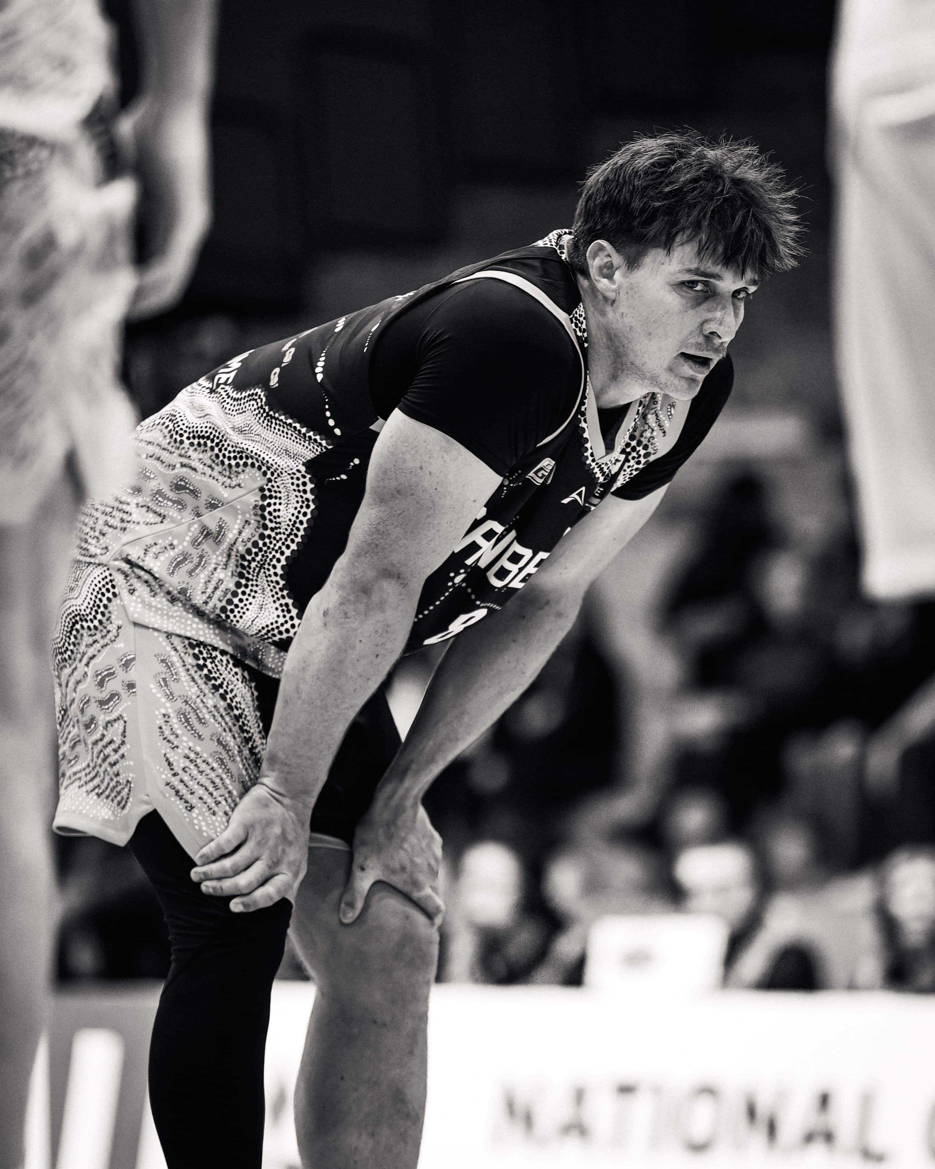 A Gunners player bends with hands on knees, spent, in the Indigenous round jersey