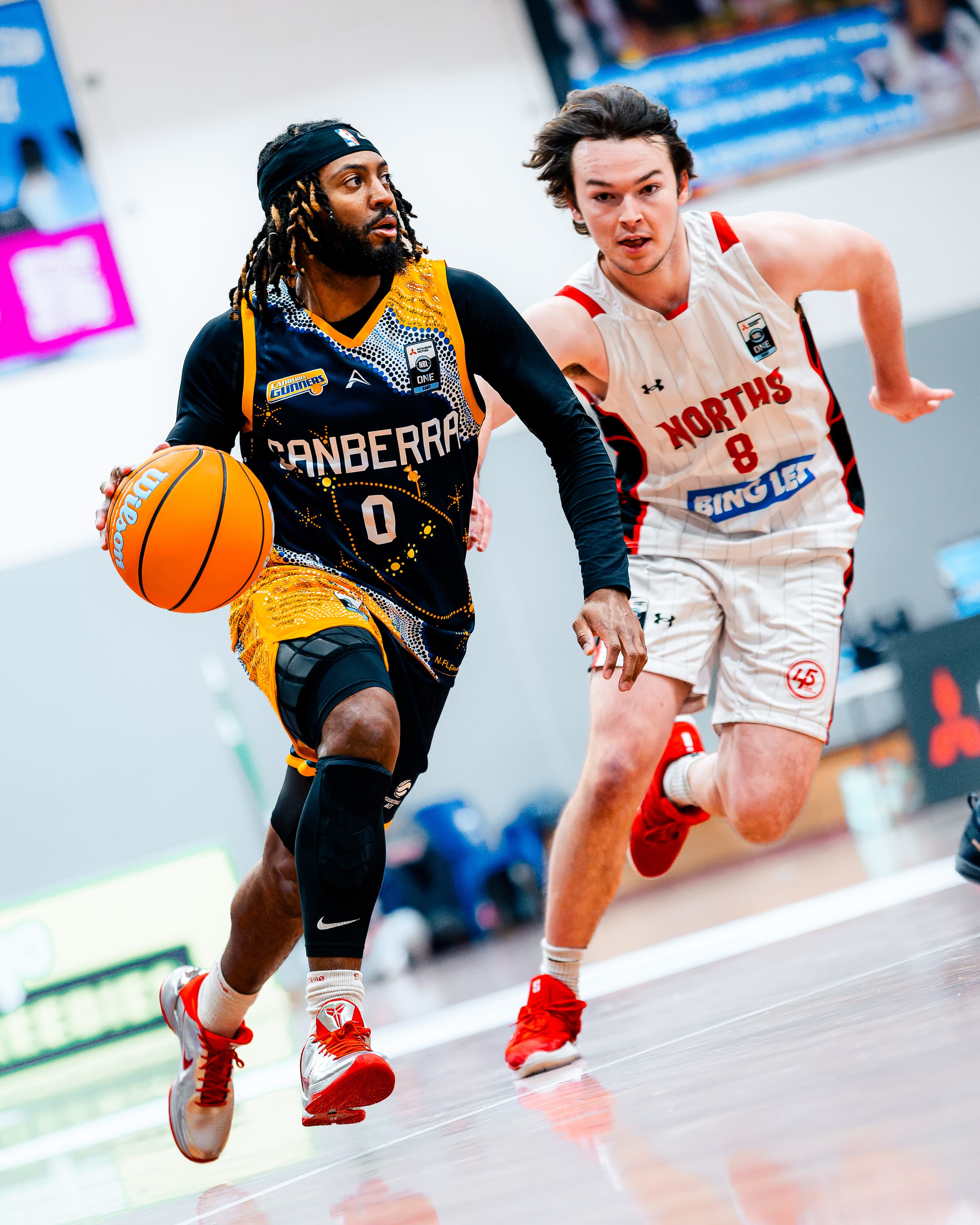 A Canberra Gunners guard pushes the ball up the floor ahead of a Norths defender