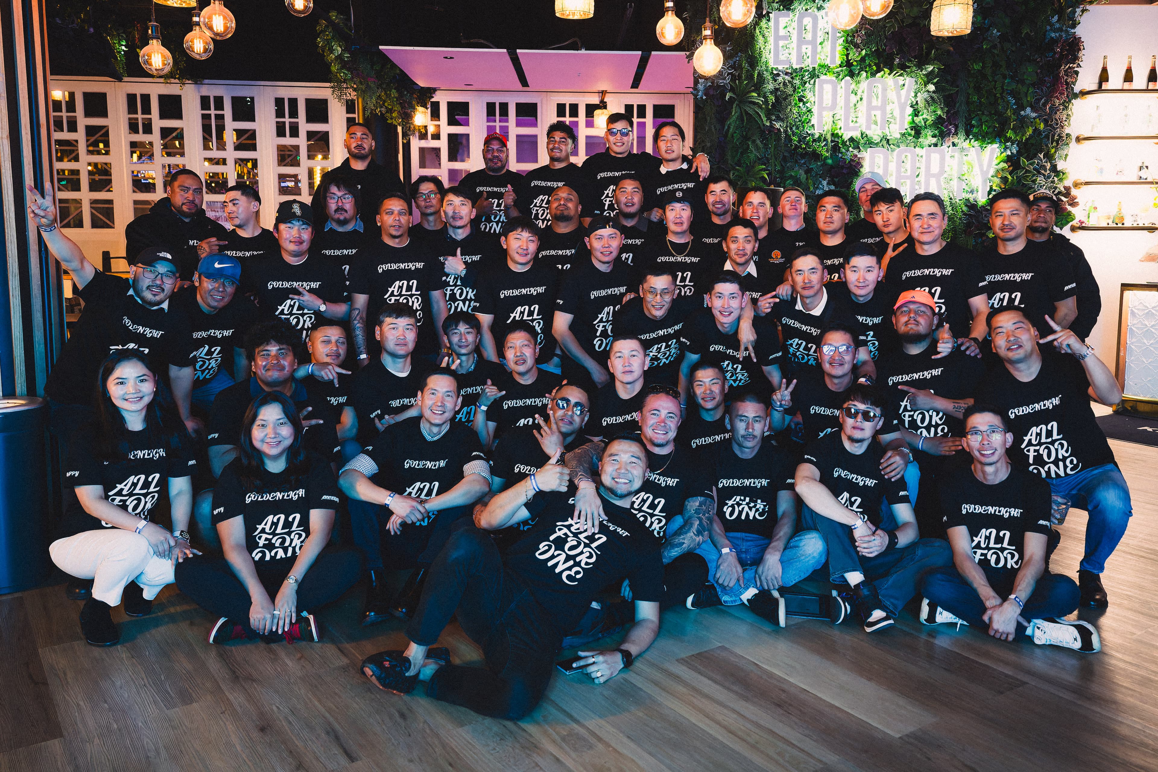 The Golden Light Group team together under the festoon lights in their All For One tees