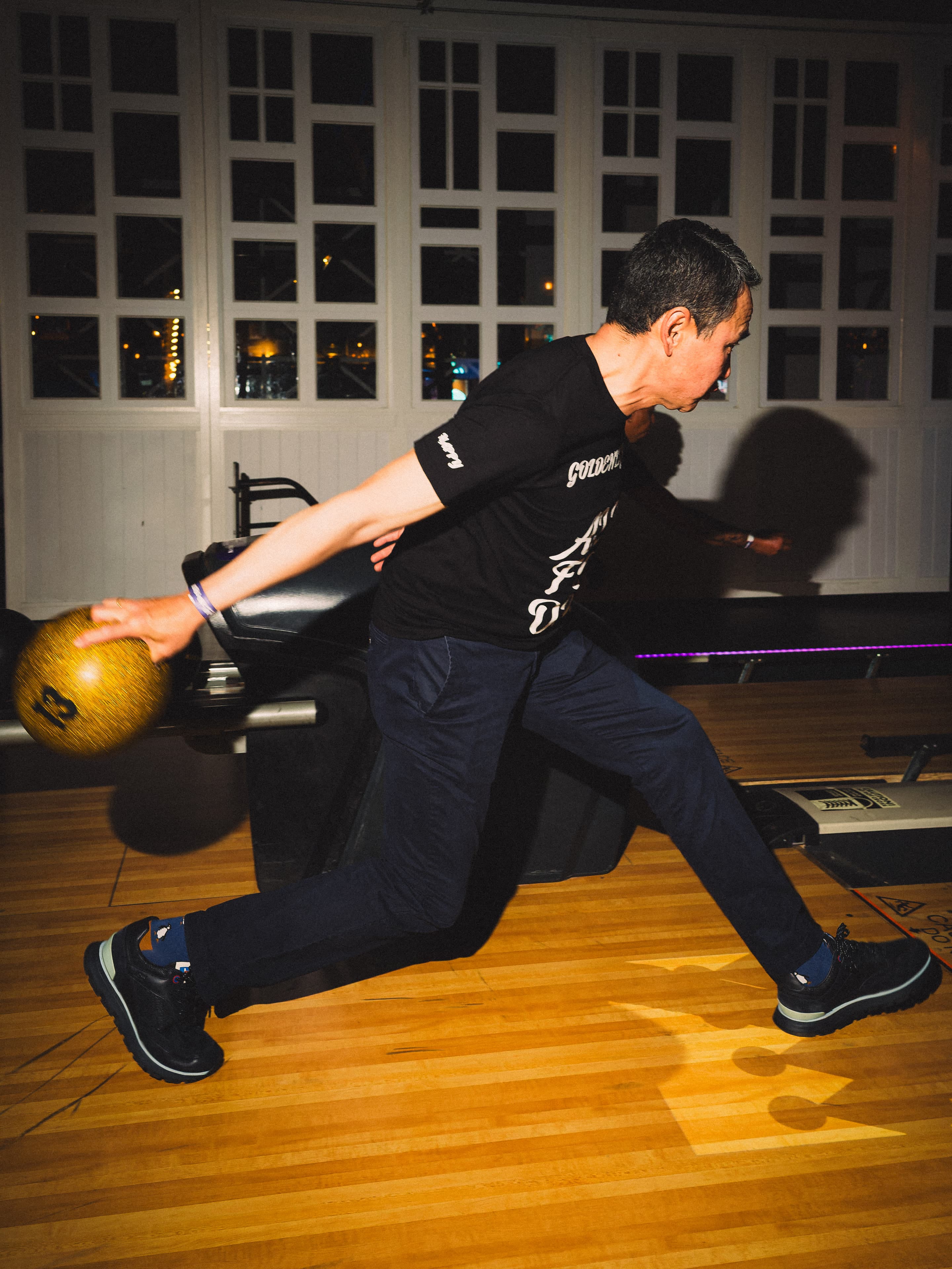 A bowler strides in with a gold ball, arm swung back, the lanes off to the right