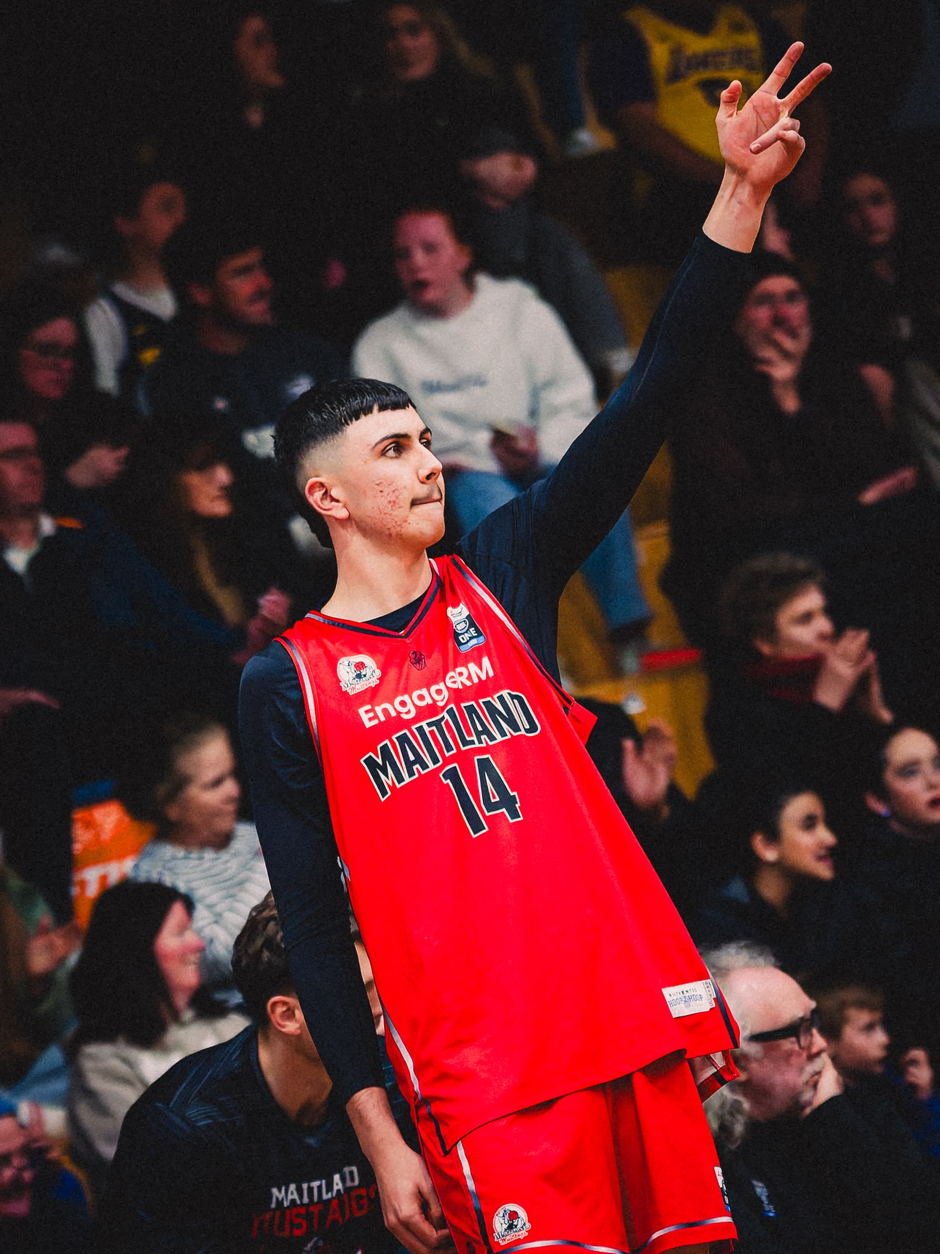 Maitland Mustangs number 14 holds up three fingers after a three pointer, packed grandstand behind him