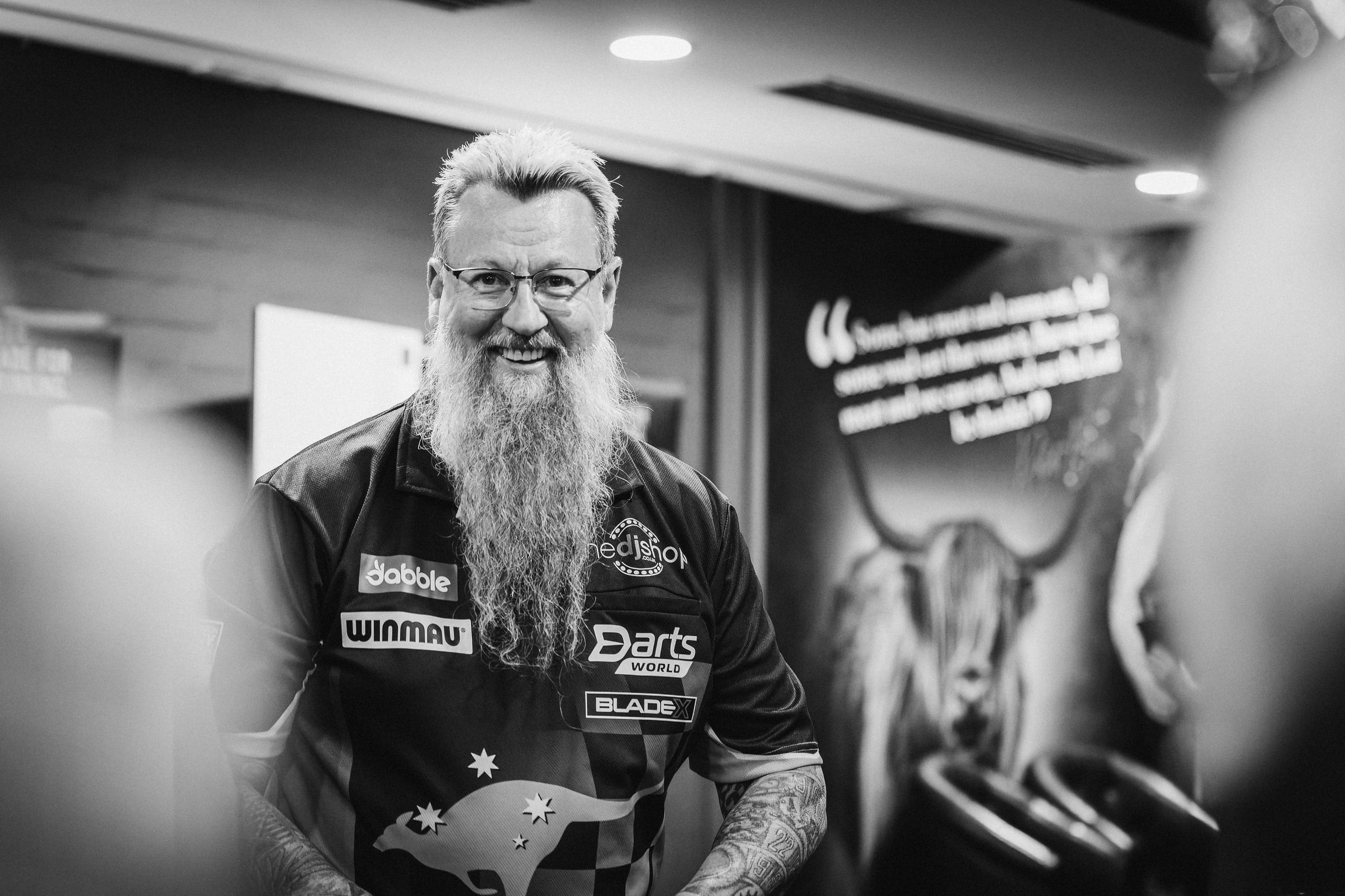 Black and white portrait of a darts player with a long beard and glasses
