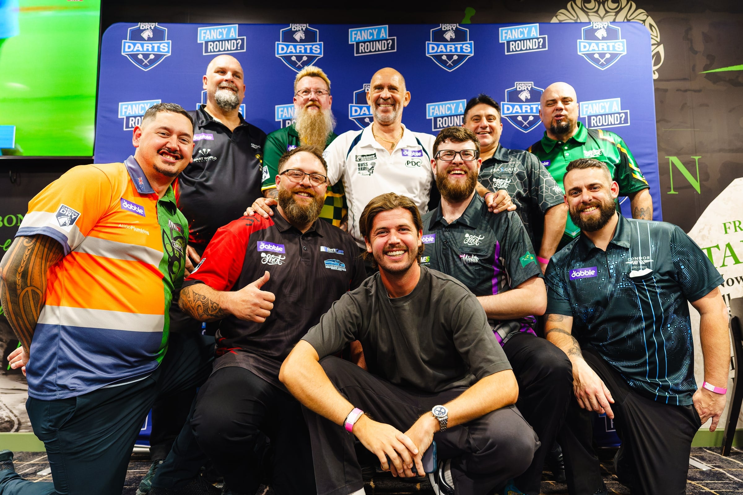 A group portrait in front of the Carlton Dry darts backdrop