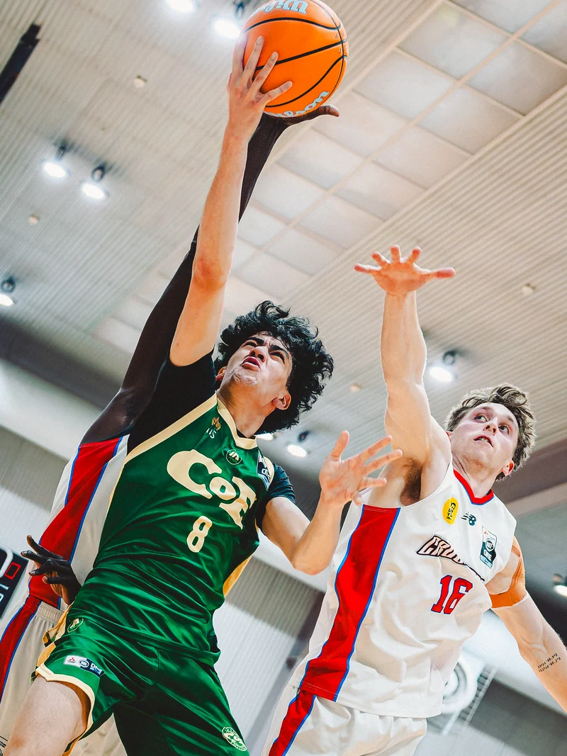 A basketball player reaching for the basket over a defender