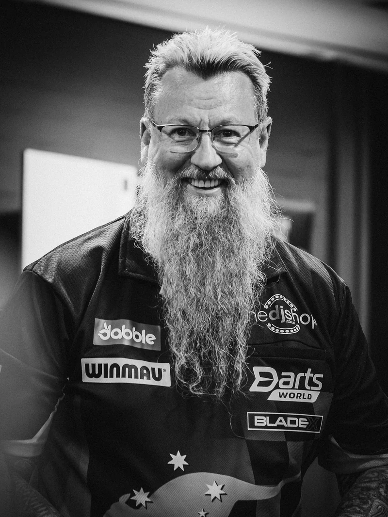 Black and white portrait of a smiling bearded darts player