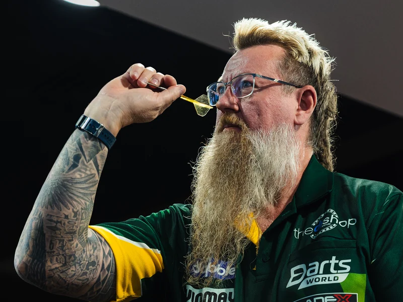 A bearded darts player concentrating as he lines up a throw