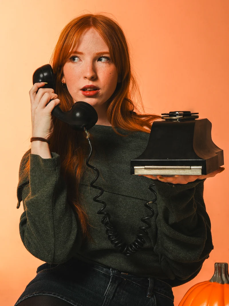 Studio portrait holding a vintage telephone against an orange backdrop
