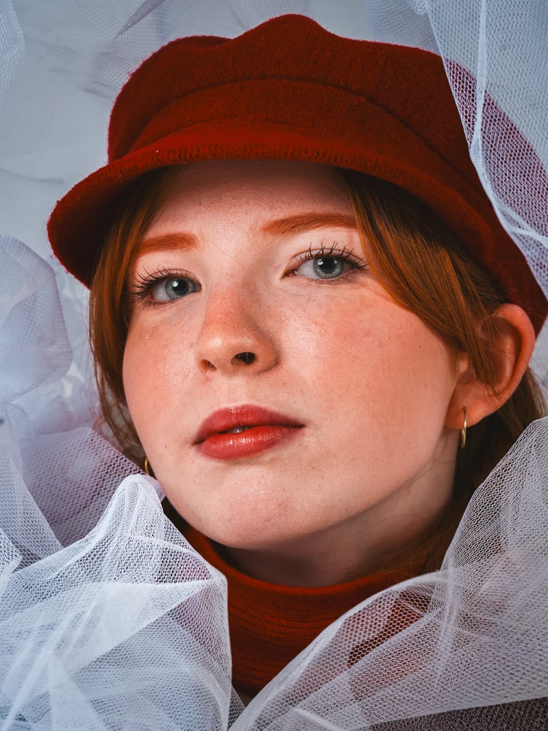 Close portrait in a red cap framed by white fabric