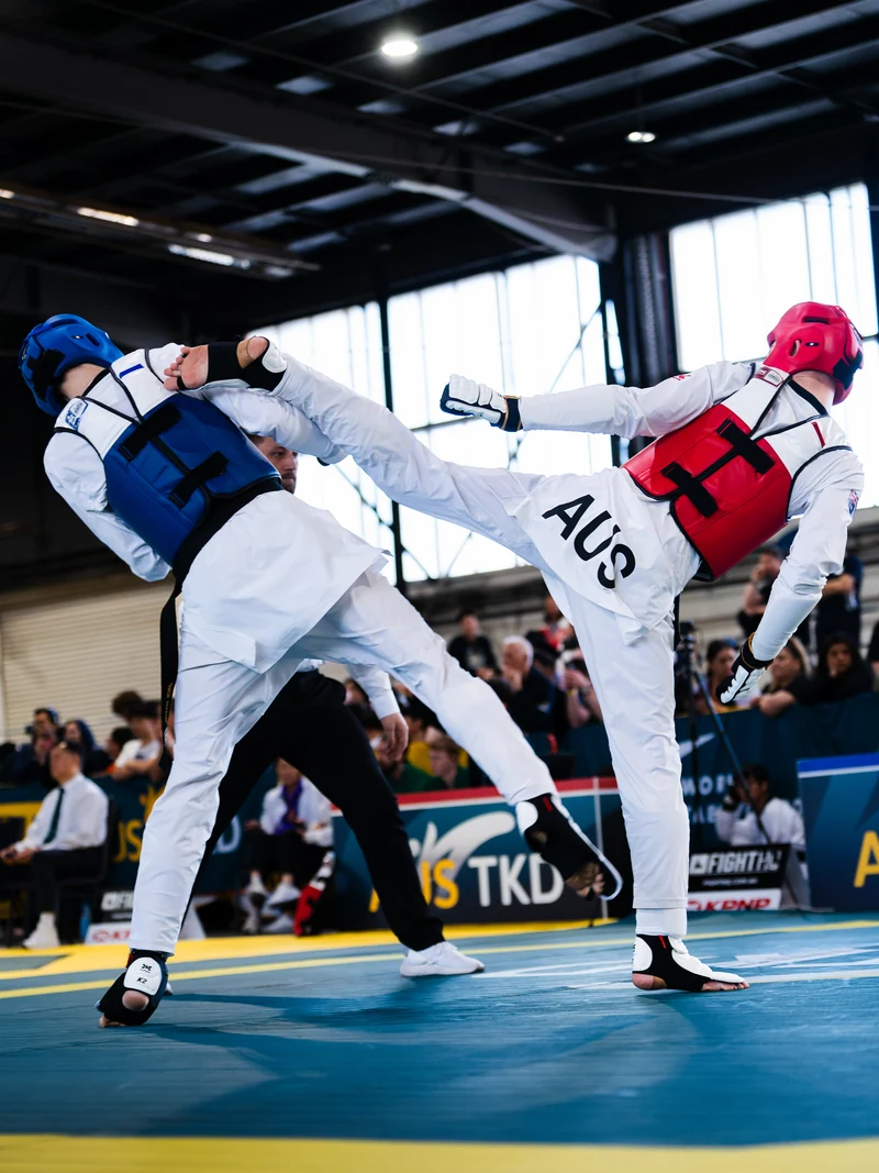 Two Taekwondo athletes exchanging high kicks at close range