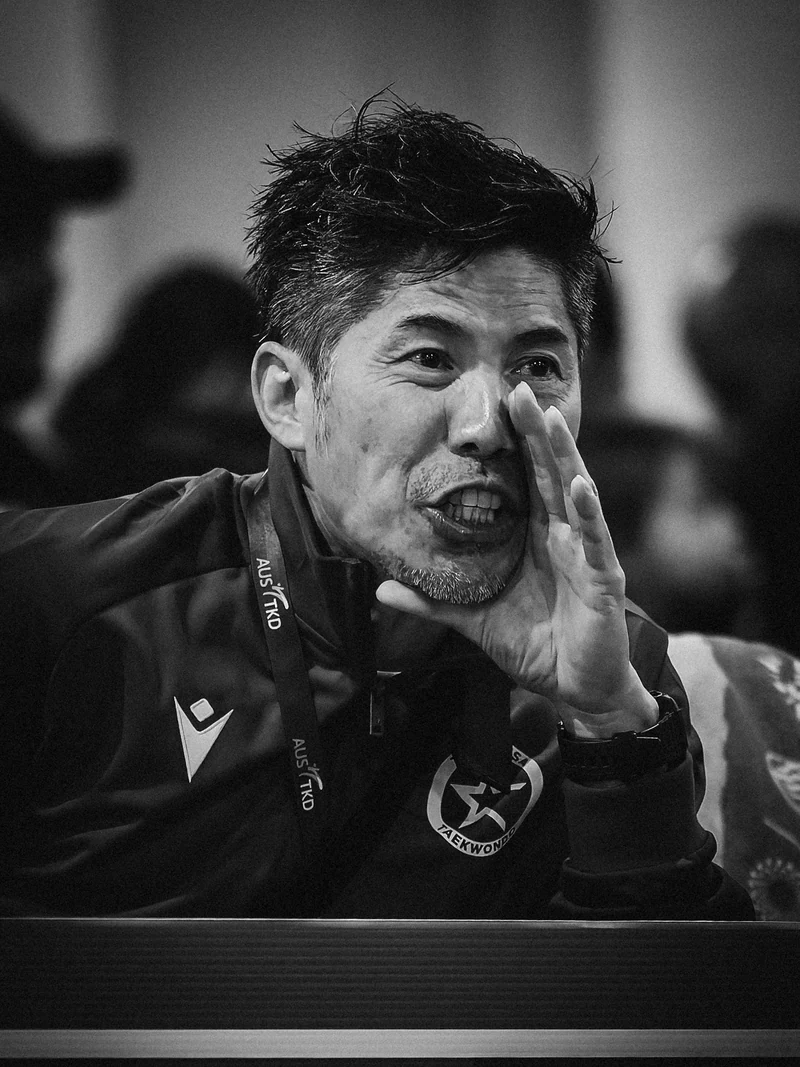 Black and white close-up of a man cupping a hand beside his mouth at the sideline