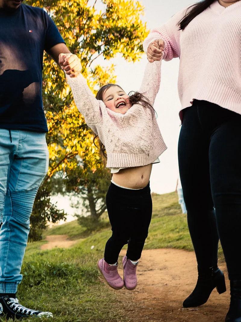 A laughing child being lifted by the hands between two adults