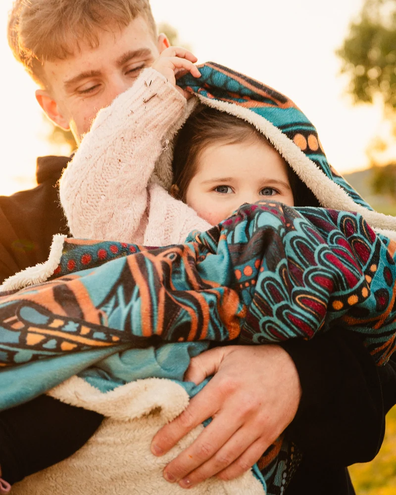 A child peeking out from a colourful blanket while being held