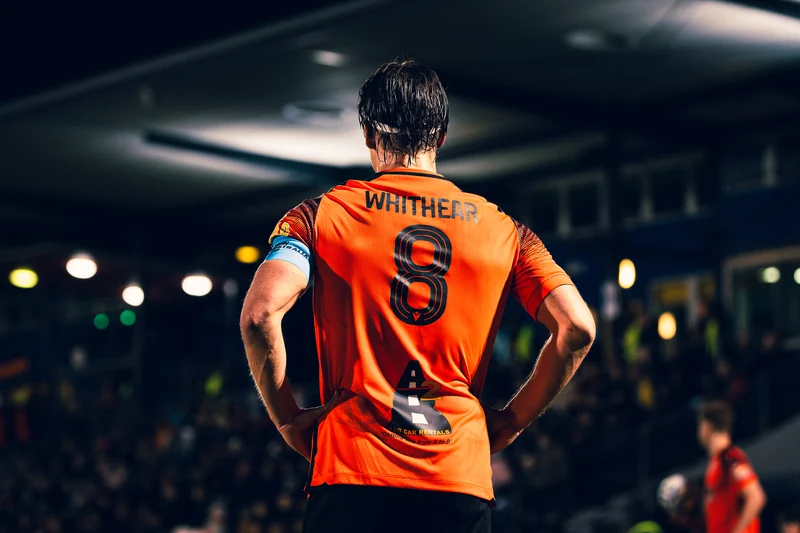 A football player in an orange number eight shirt beneath stadium lights