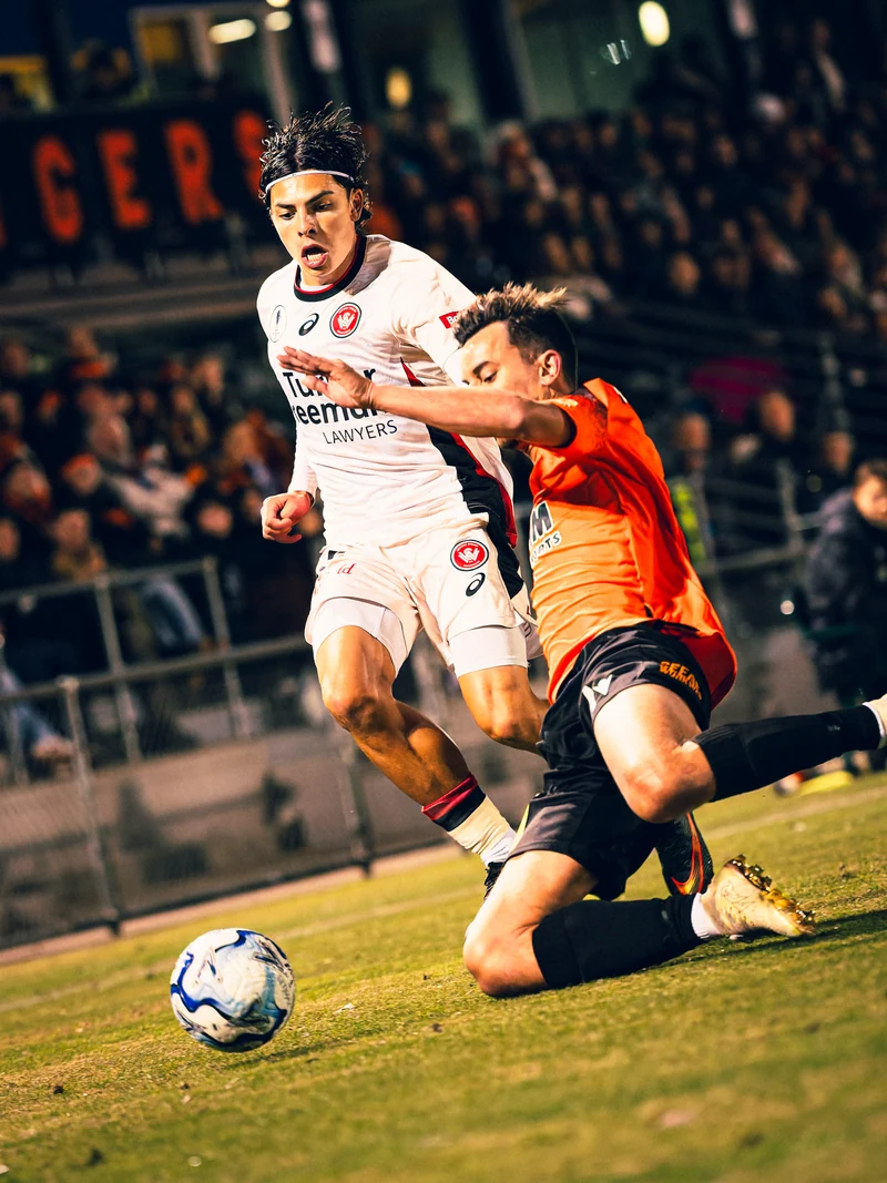 A football player sliding towards the ball beside an opponent