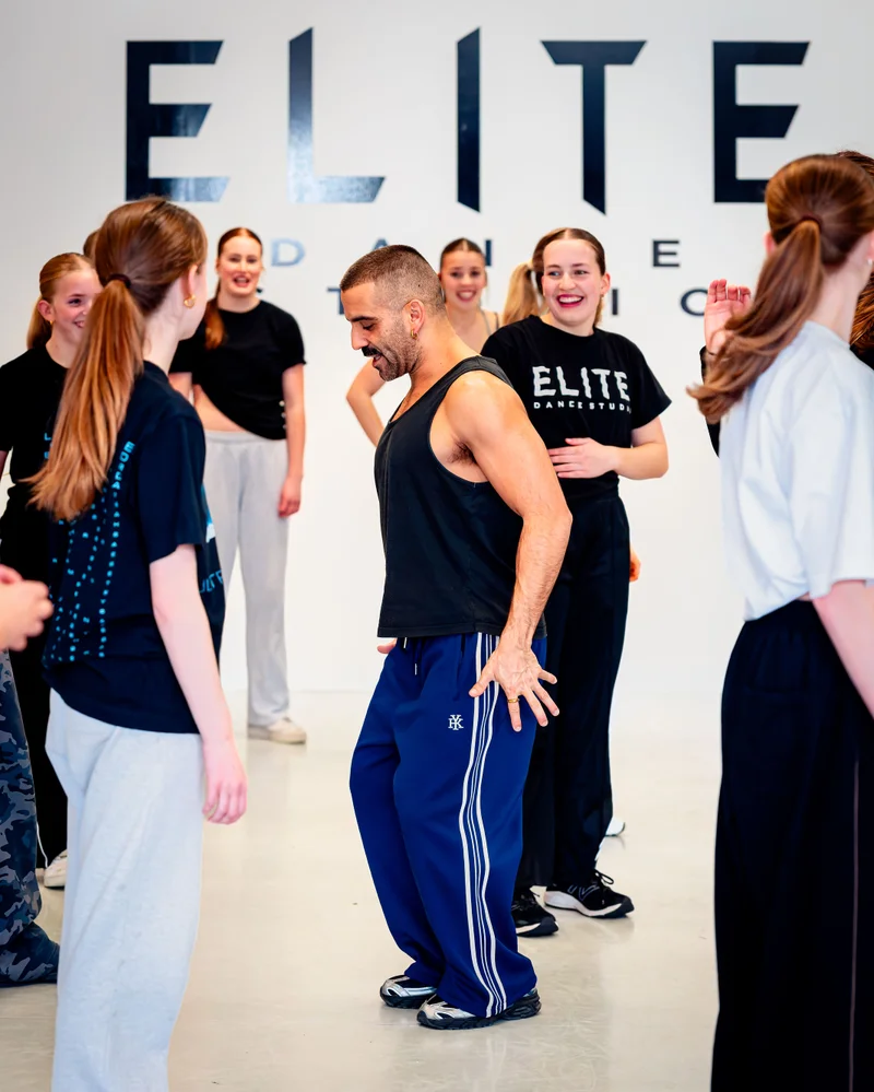 Stephen Tannos coaching dancers beside the Elite Dance Studios wall sign