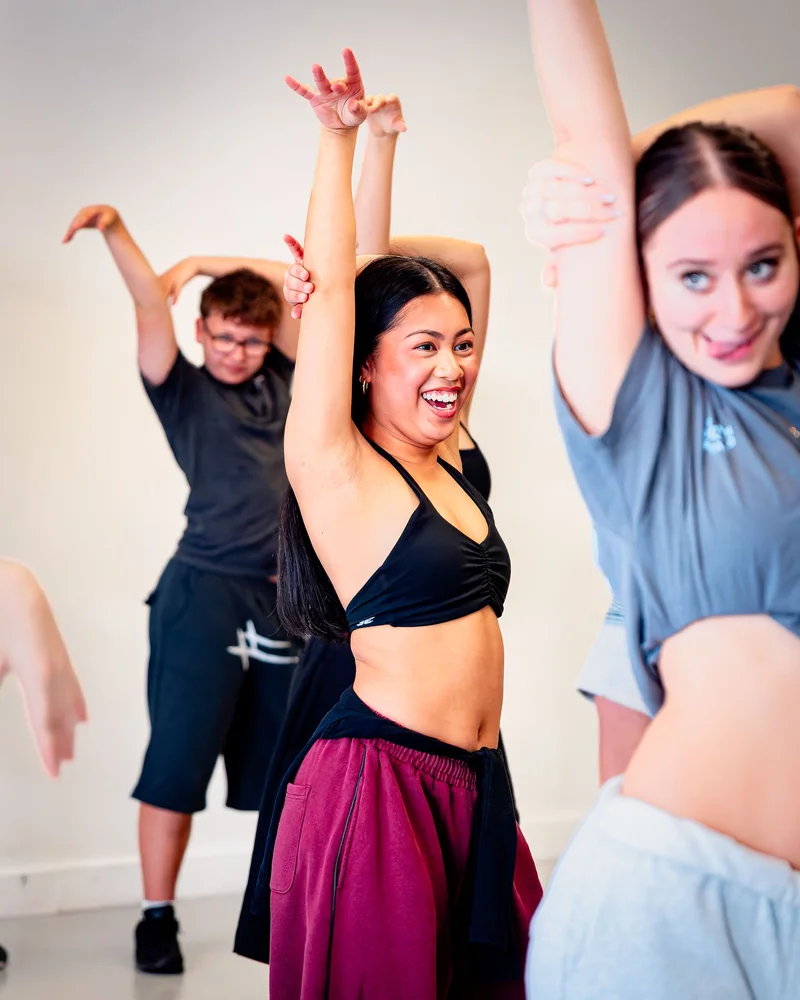 Dancers smiling with their arms raised during a studio class