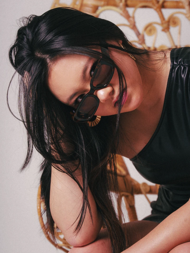 Leaning forward on a wicker chair, looking over sunglasses