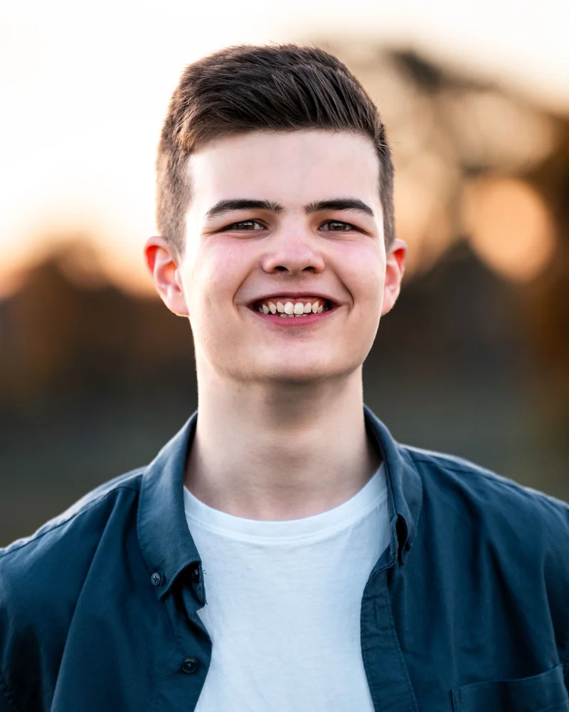 Outdoor headshot of James smiling, with warm light behind him