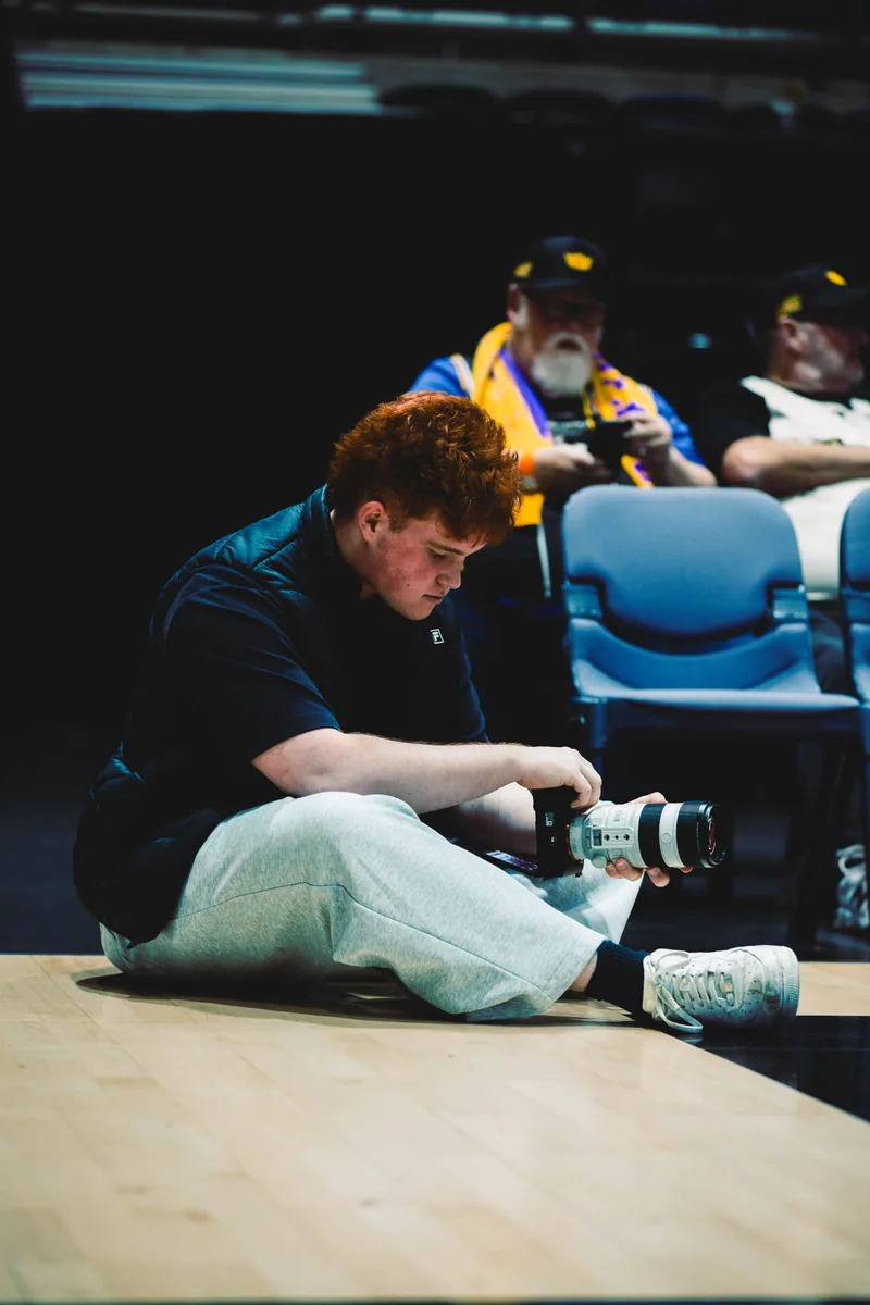 Kian checking his camera while sitting beside the basketball court