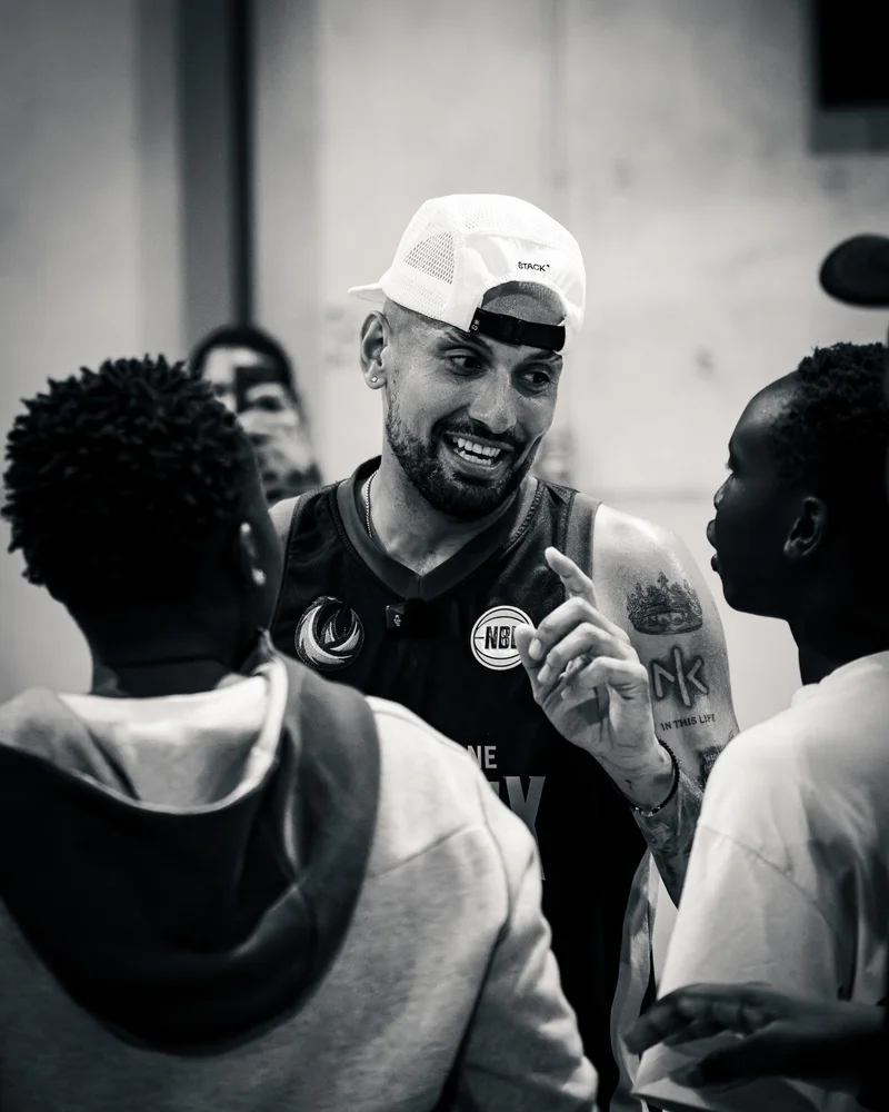 Nick Kyrgios talking with young basketball players at Takeover AUS, in black and white