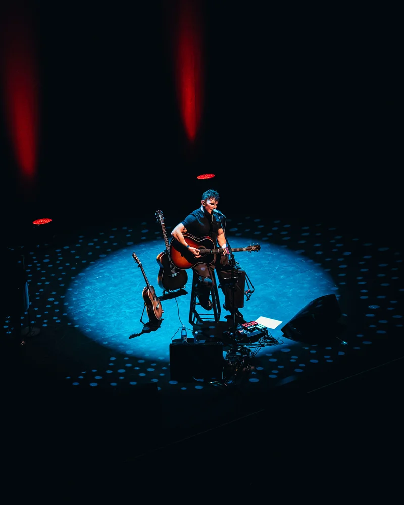Michael Paynter playing guitar in a pool of blue stage light beneath red lights