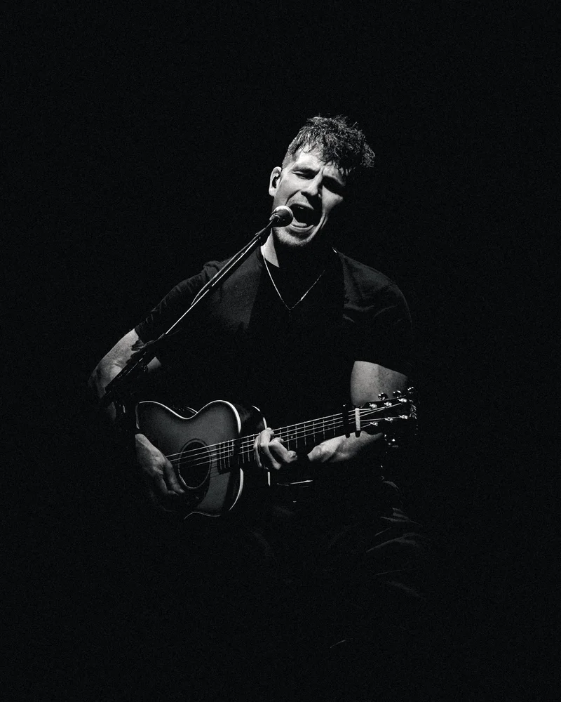 Michael Paynter singing and playing acoustic guitar, in black and white