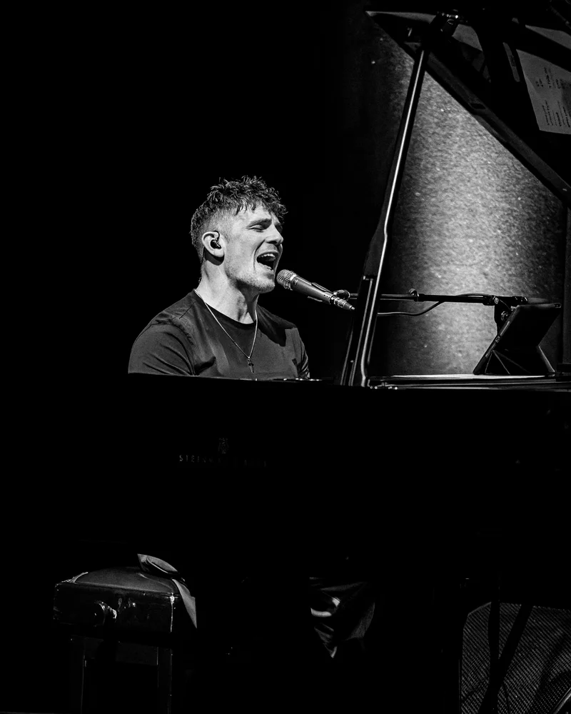 Michael Paynter singing at a grand piano, in black and white